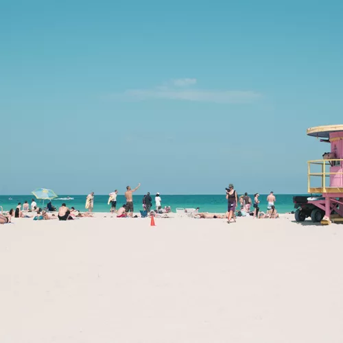 People relaxing on Miami Beach beside the iconic pastel lifeguard tower, enjoying the white sand and turquoise Atlantic Ocean - Contiki Miami to Dallas Tour