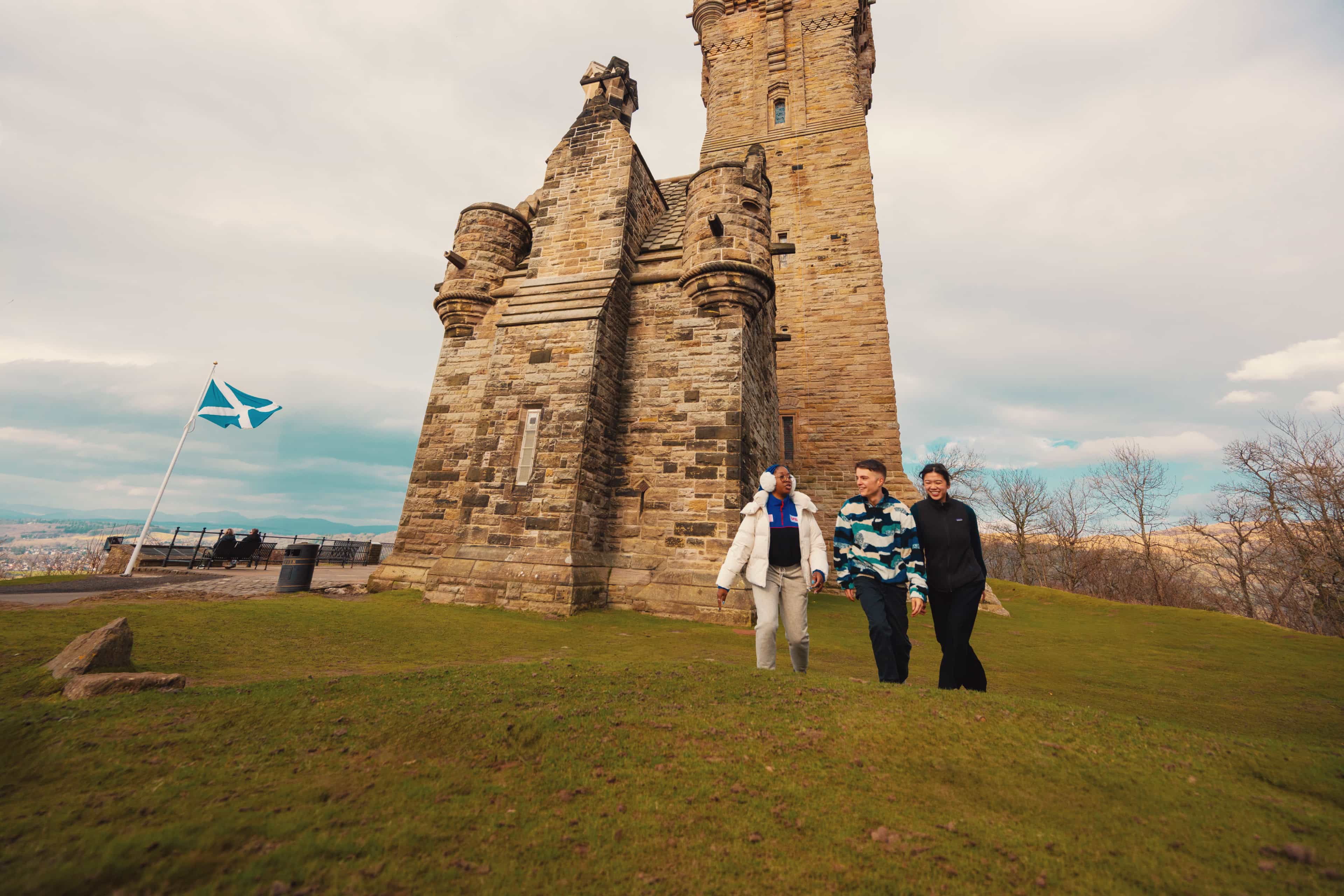 Travellers walking across the grounds of the National Wallace Monument beneath a Scottish flag, Stirling, Scotland.