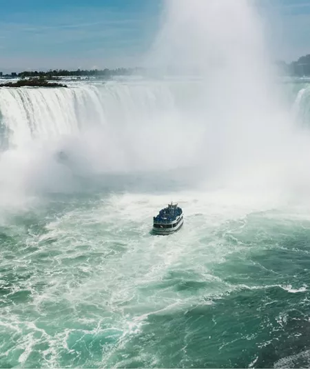 Boat sails through the mist beneath Niagara Falls on Contiki's Canada: Toronto, Niagara & Quebec Tour, experiencing one of Canada's most iconic natural wonders