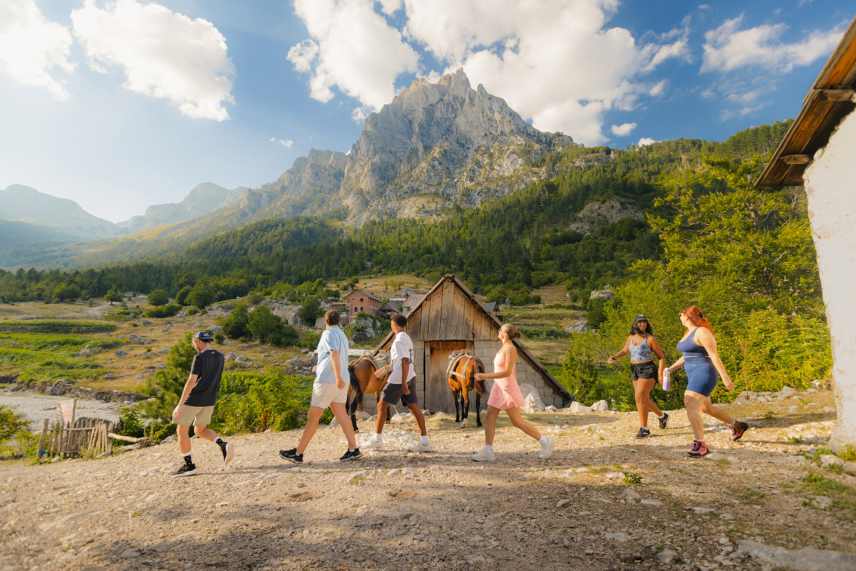 Group Hiking Past A Cabin And Horse In Valbona Valley Albanian Alps