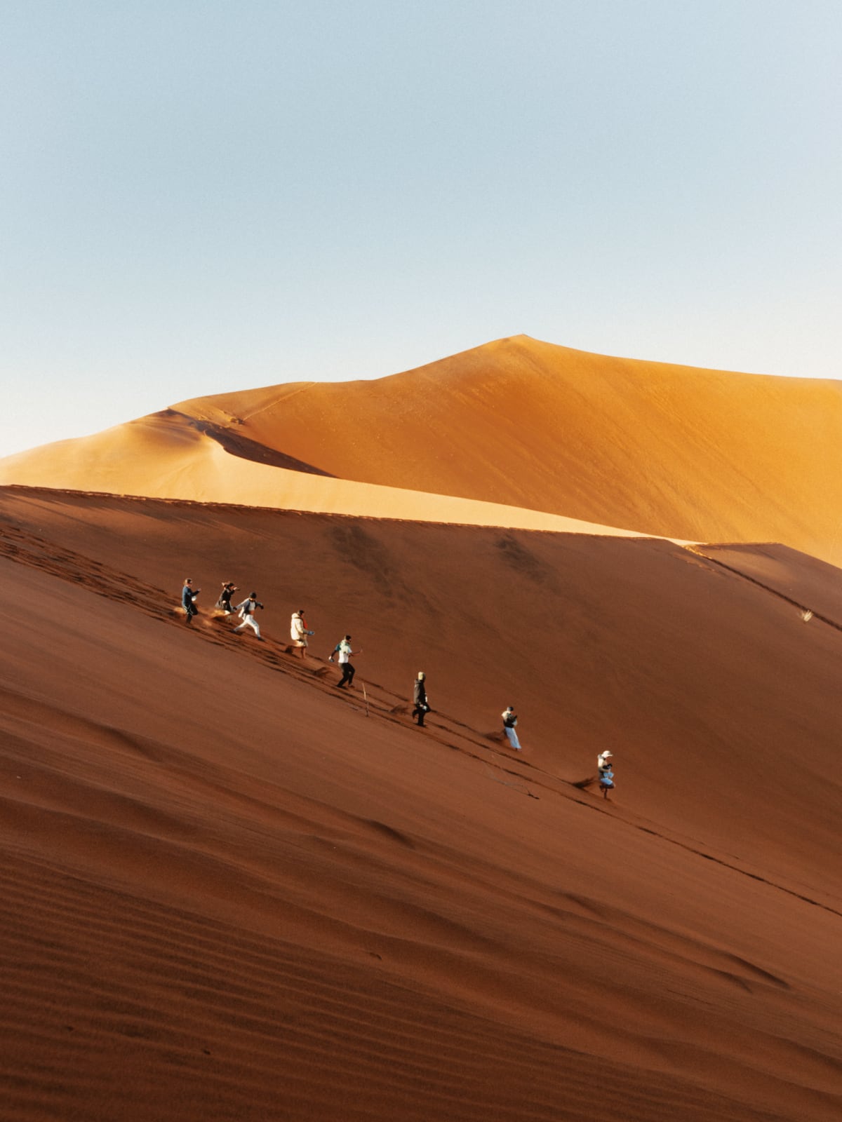 Travellers hiking in a line along the ridge of towering red sand dunes in Namibia.