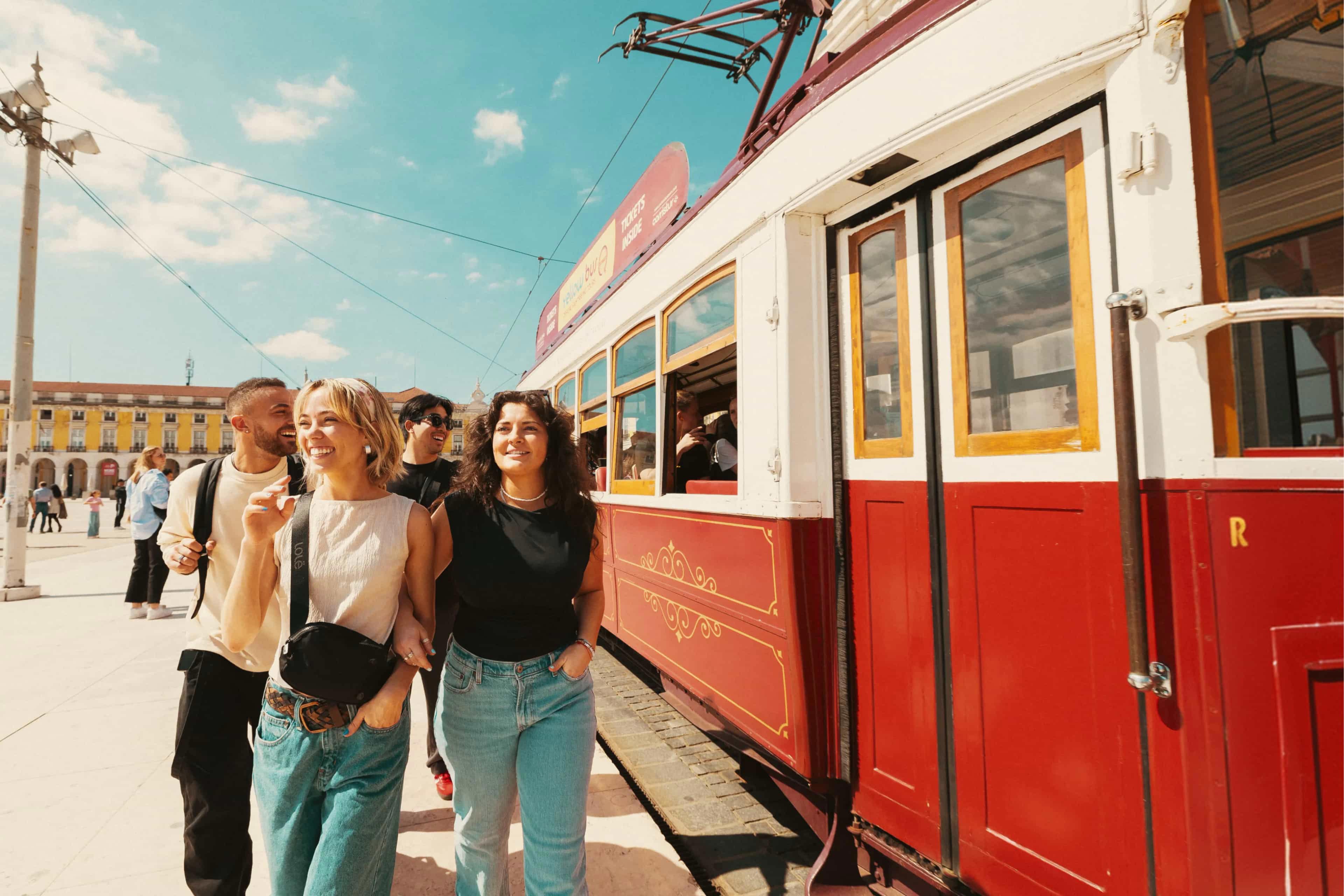Travellers walking beside a traditional red tram in Lisbon, Portugal.