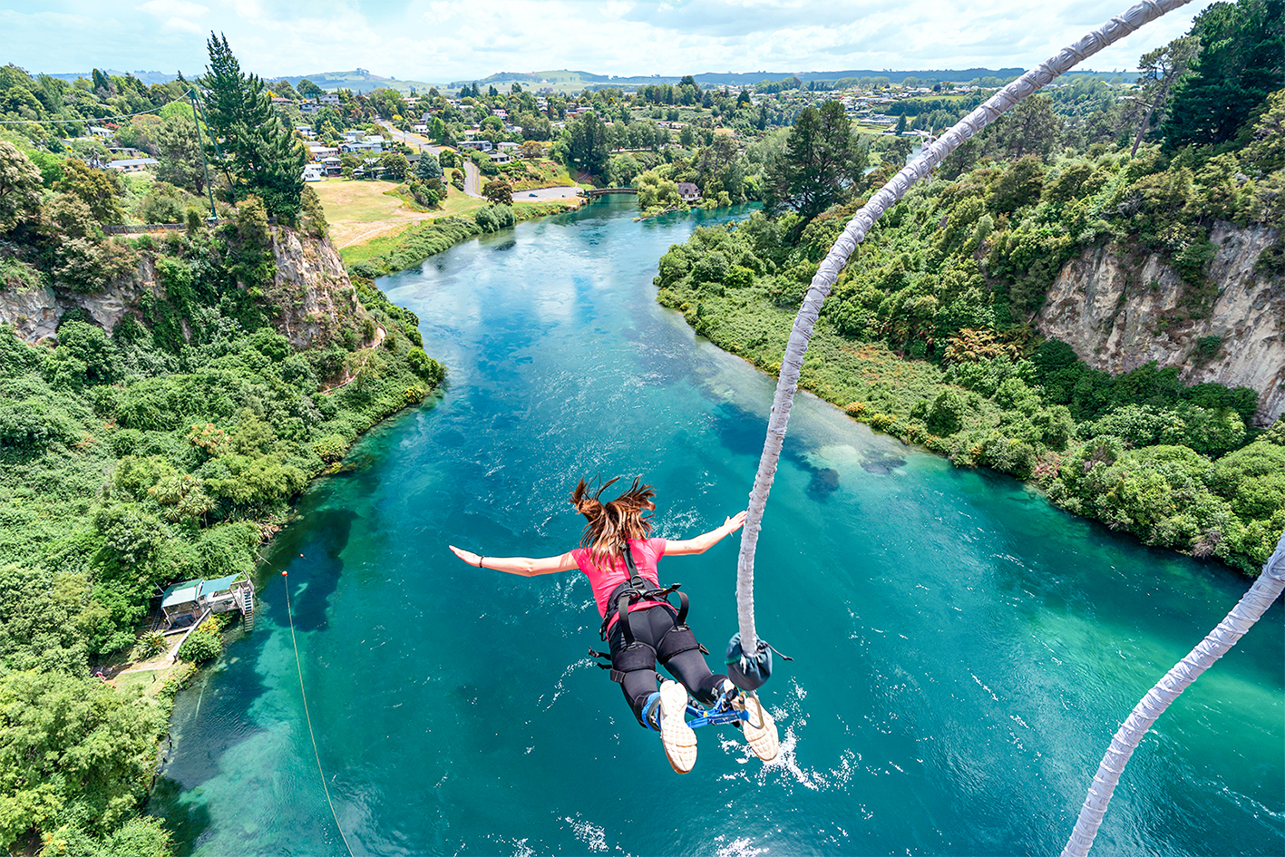 Traveller mid fall during a bungy jump over a blue river, Taupō, New Zealand