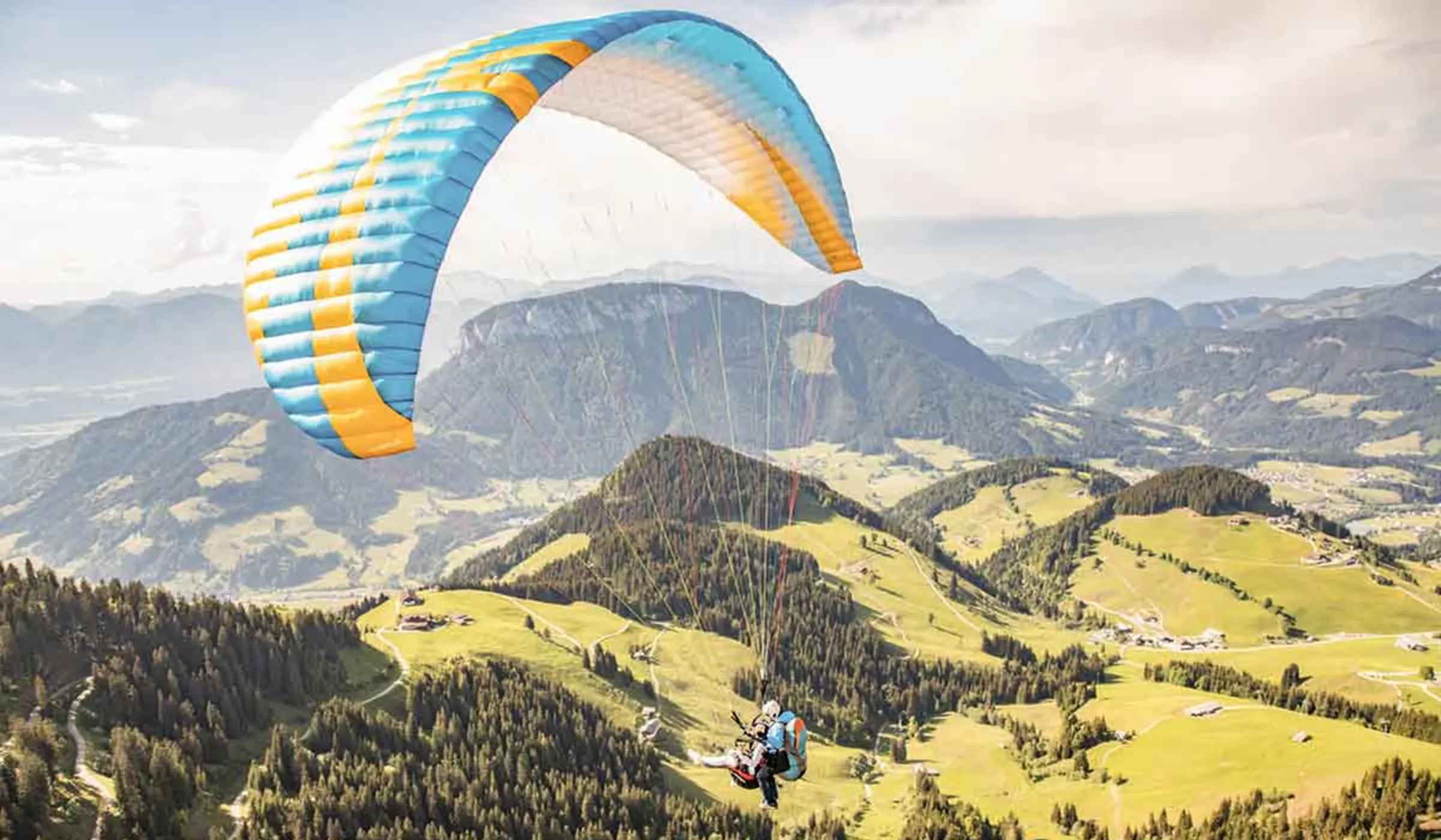 Two people paragliding over mountains, forests and meadows 