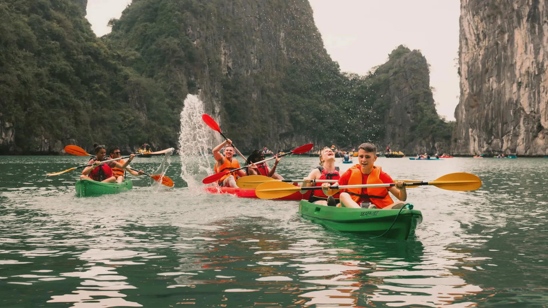 Young travellers kayaking between towering limestone karsts in Ha Long Bay Vietnam - Contiki Best of Vietnam Tour