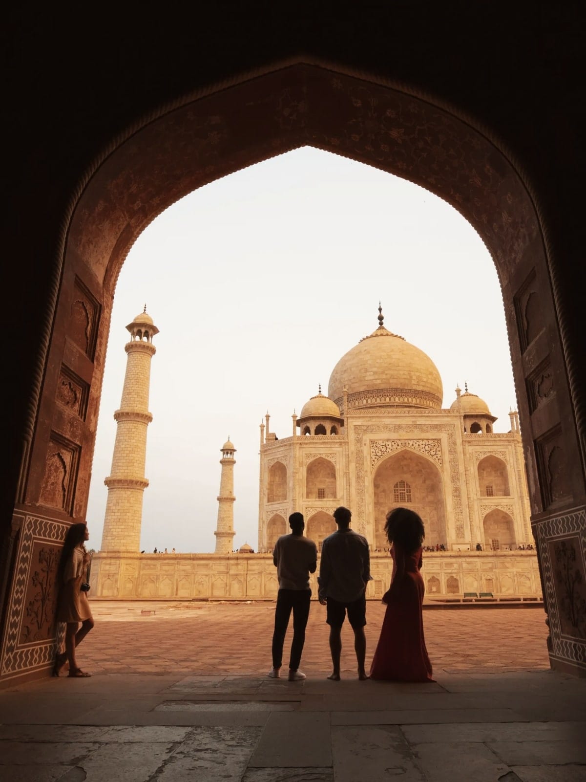 Travellers stand silhouetted beneath an archway, admiring the Taj Mahal in Agra, India.