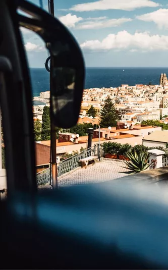 View from a coach overlooking the coastal town of Cefalù in Sicily, with terracotta rooftops, dramatic cliffs and the Mediterranean Sea beyond - Sicily Escape Tour