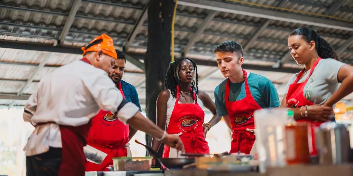 A group of young people learning how to cook from a chef in Thailand.