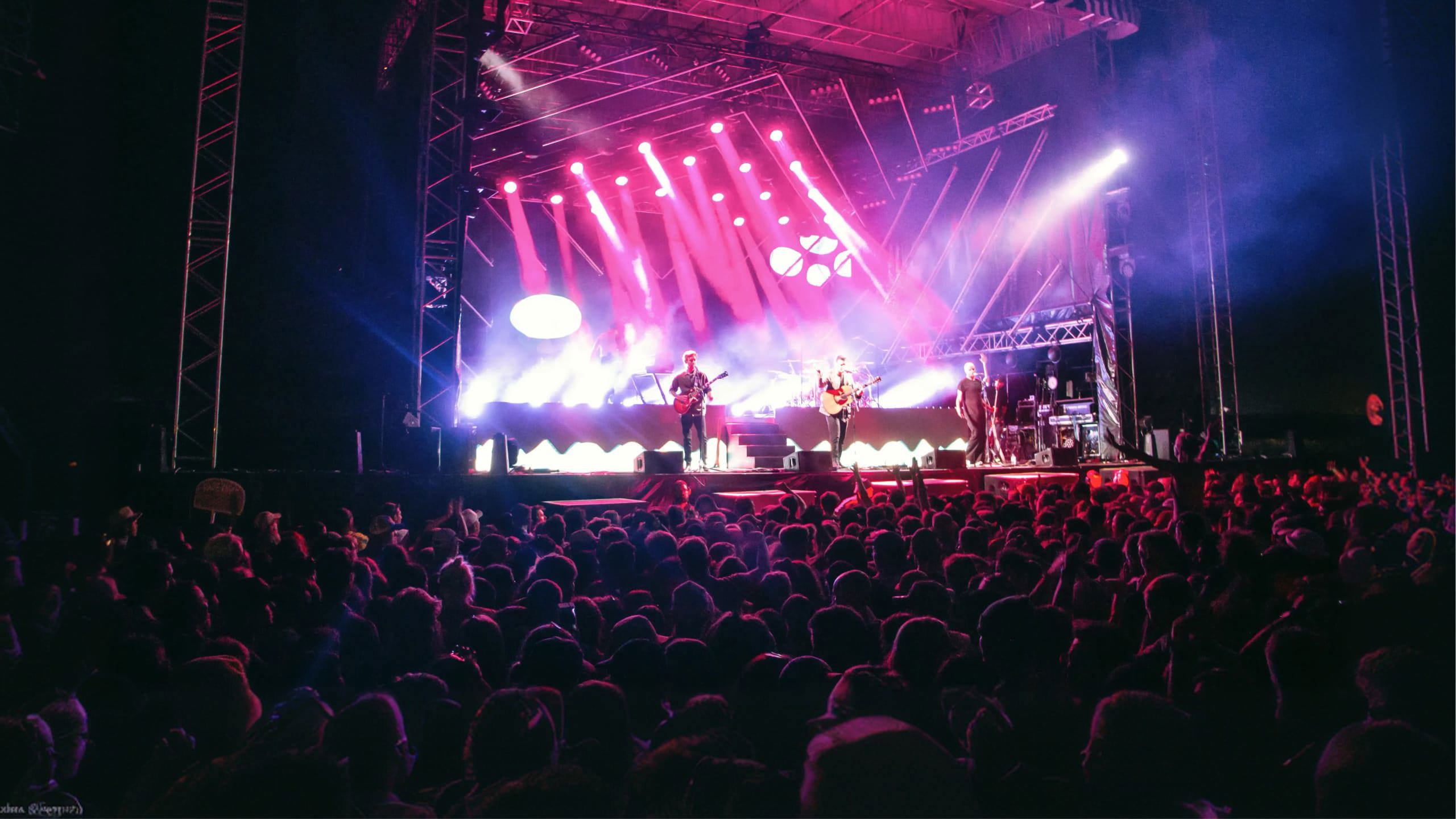 Live band performing on stage with dramatic pink and purple lighting to a large crowd at Rhythm and Alps music festival in New Zealand - Contiki NZ Festival Tour
