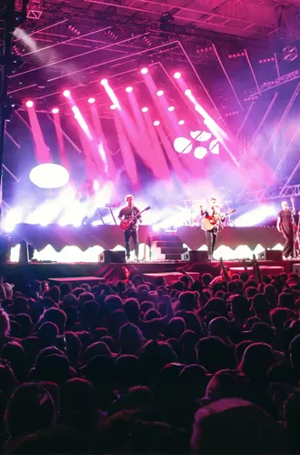 Live band performing on stage with dramatic pink and purple lighting to a large crowd at Rhythm and Alps music festival in New Zealand - Contiki NZ Festival Tour