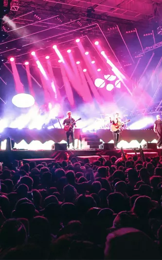 Live band performing on stage with dramatic pink and purple lighting to a large crowd at Rhythm and Alps music festival in New Zealand - Contiki NZ Festival Tour