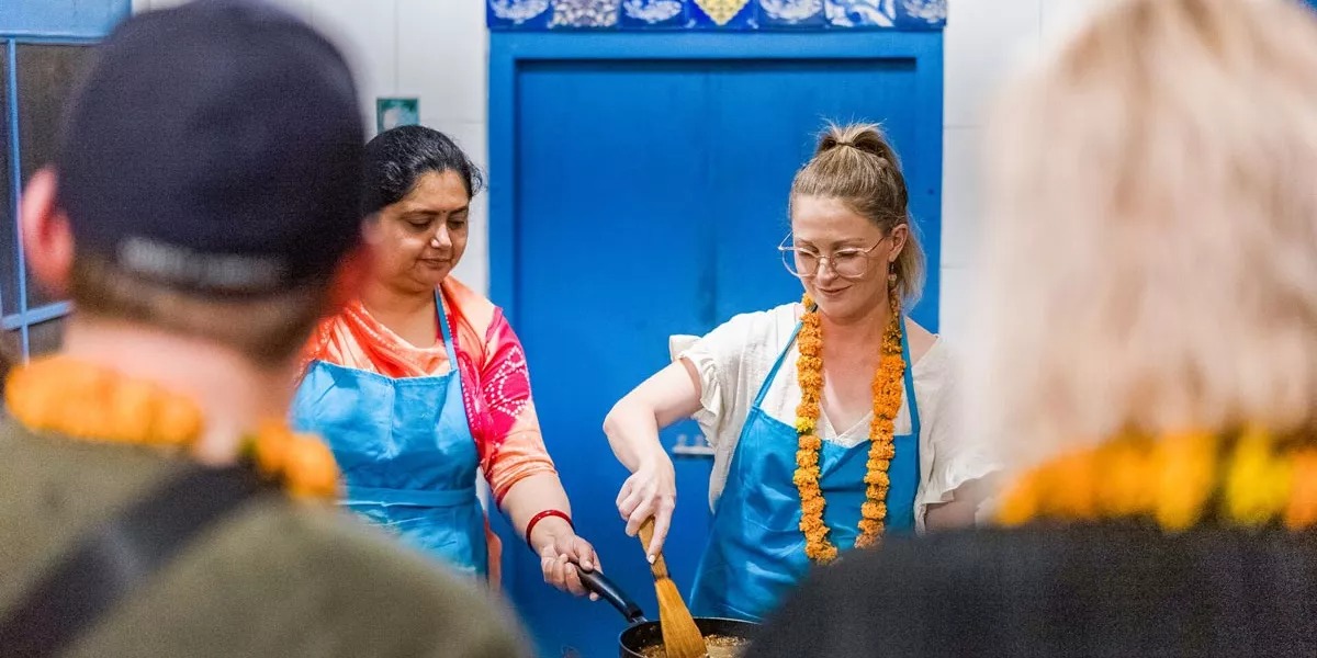 A woman learning to cook from a local person in India.