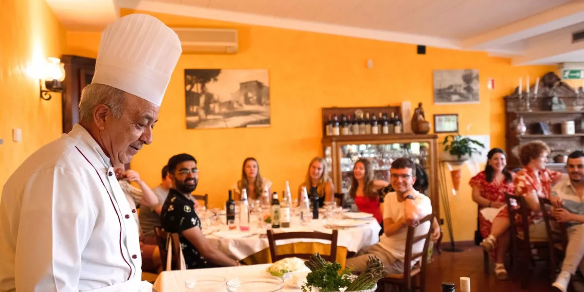 The chef is talking to a young group of people in his restaurant in Italy.