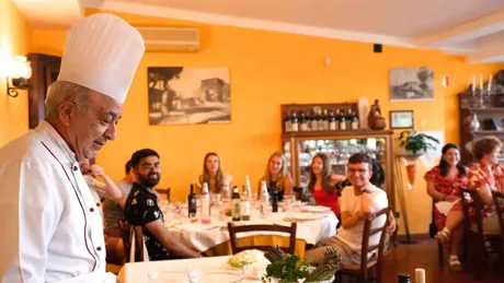 The chef is talking to a young group of people in his restaurant in Italy.