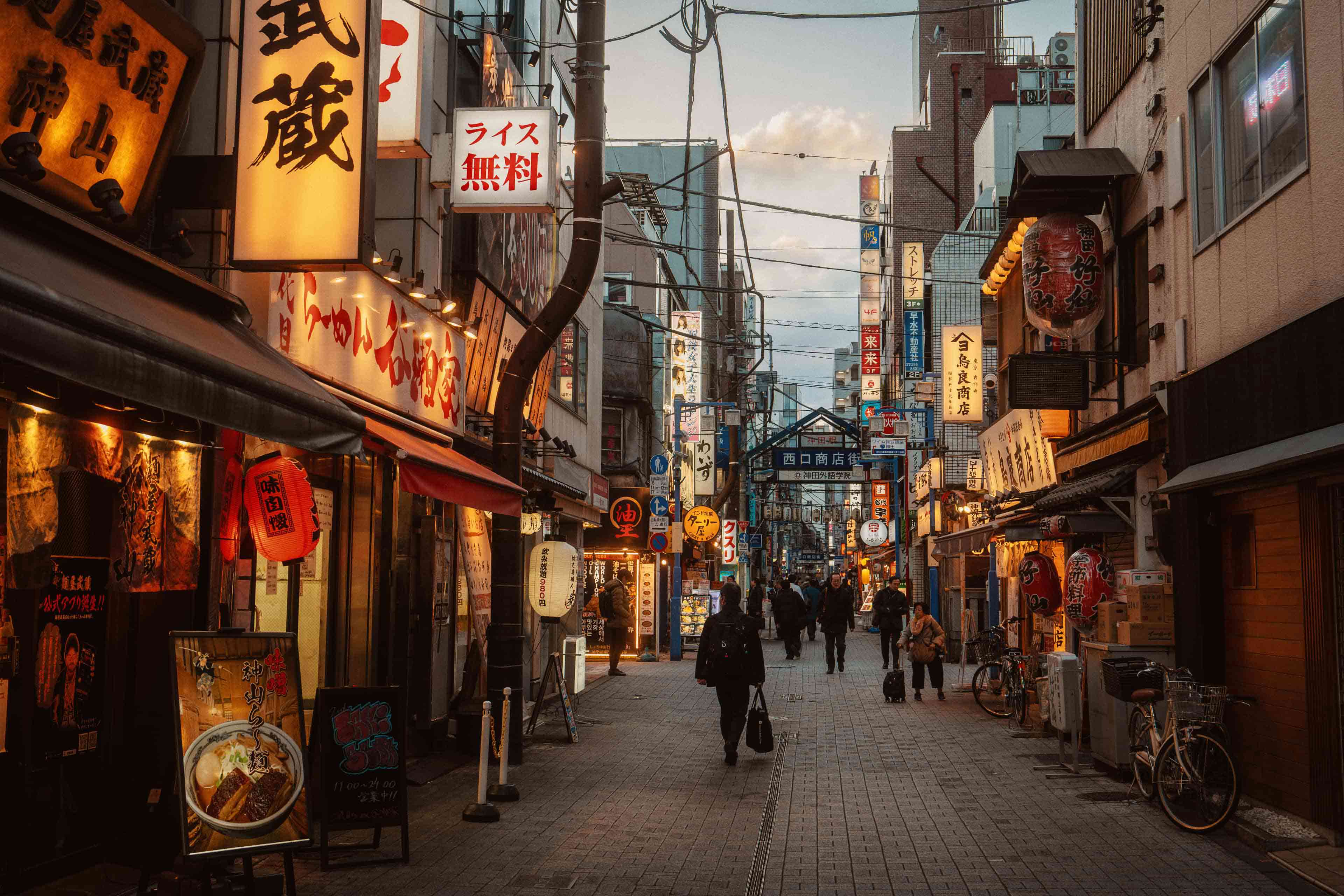 A narrow lantern-lit street lined with signage and ramen shops in Tokyo, Japan.