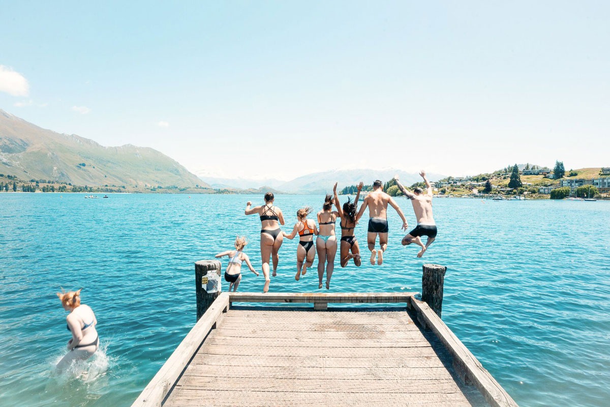 A group of friends jumping off into the lake mountains around the lake in New Zealand.
