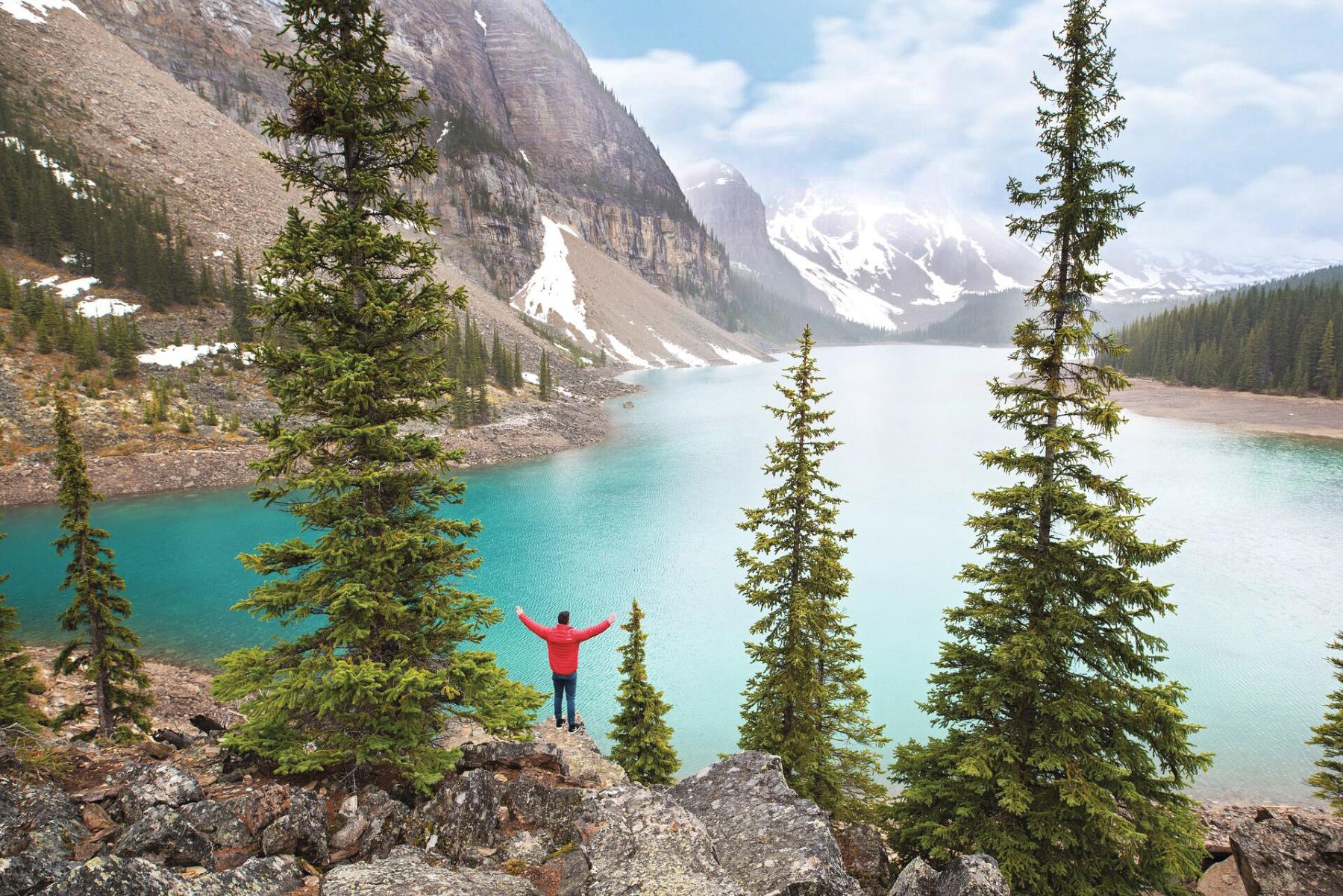 Tourist in red jacket standing in front of Moraine Lake in Banff National Park in Canada