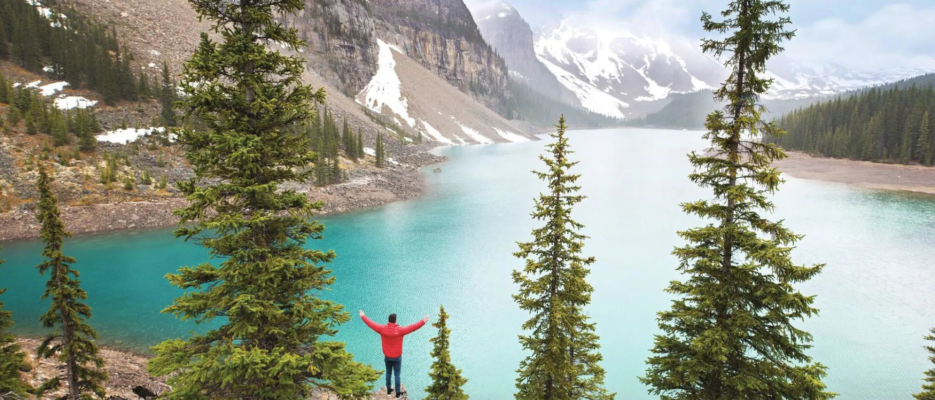 Tourist in red jacket standing in front of Moraine Lake in Banff National Park in Canada