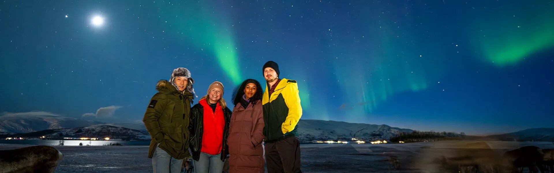 A group of young people standing outside in the snow with the northern lights in Norway.