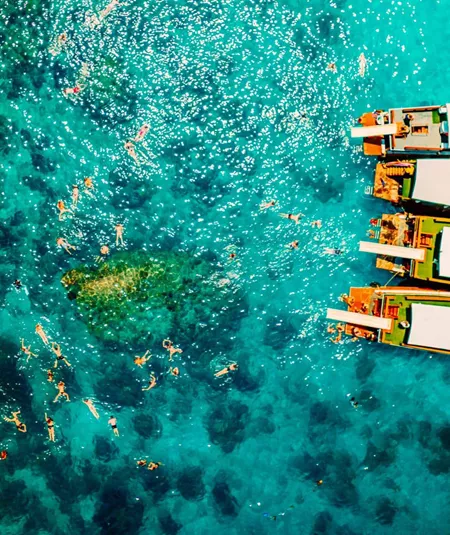Contiki travellers swimming and snorkelling in vivid turquoise waters around traditional wooden boats anchored off the coast of a Thai island on a Thai Island Hopper East Tour