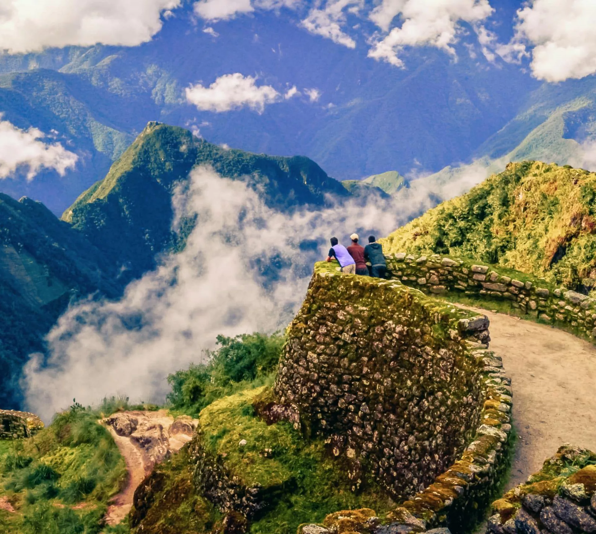 Three hikers on ancient Inca stone ruins with panoramic views of misty Andean mountains along the Inca Trail in Peru - Contiki Inca Trail Tour