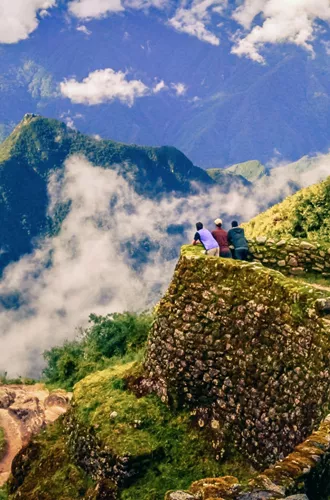 Three hikers on ancient Inca stone ruins with panoramic views of misty Andean mountains along the Inca Trail in Peru - Contiki Inca Trail Tour