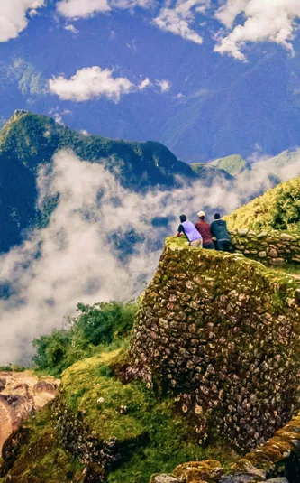 Three hikers on ancient Inca stone ruins with panoramic views of misty Andean mountains along the Inca Trail in Peru - Contiki Inca Trail Tour