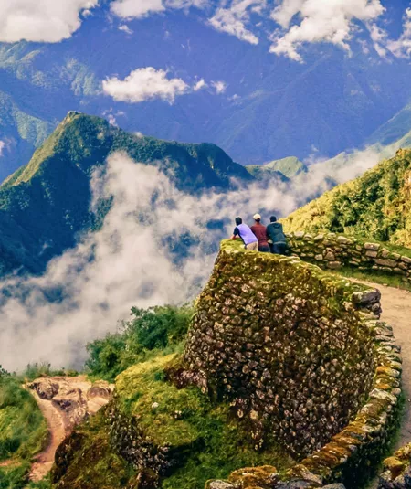 Three hikers on ancient Inca stone ruins with panoramic views of misty Andean mountains along the Inca Trail in Peru - Contiki Inca Trail Tour