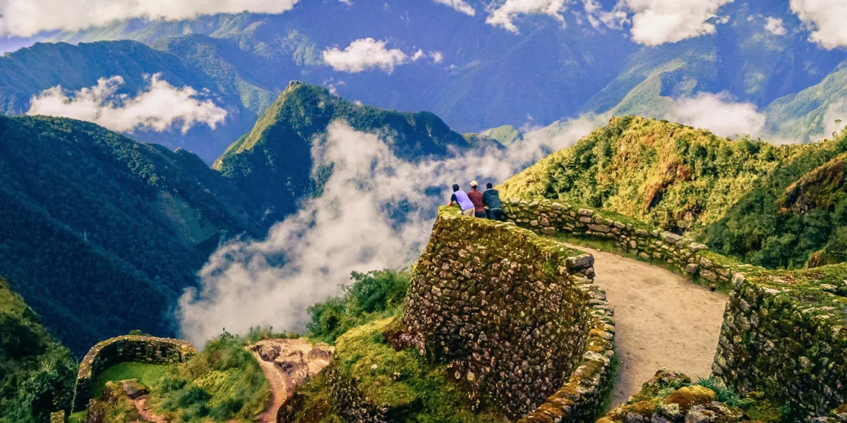 Three hikers on ancient Inca stone ruins with panoramic views of misty Andean mountains along the Inca Trail in Peru - Contiki Inca Trail Tour