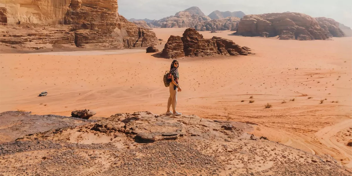Female traveller on a sandstone rock overlooking the dramatic desert landscape of Wadi Rum Valley of the Moon Jordan - Contiki Jordan Tour