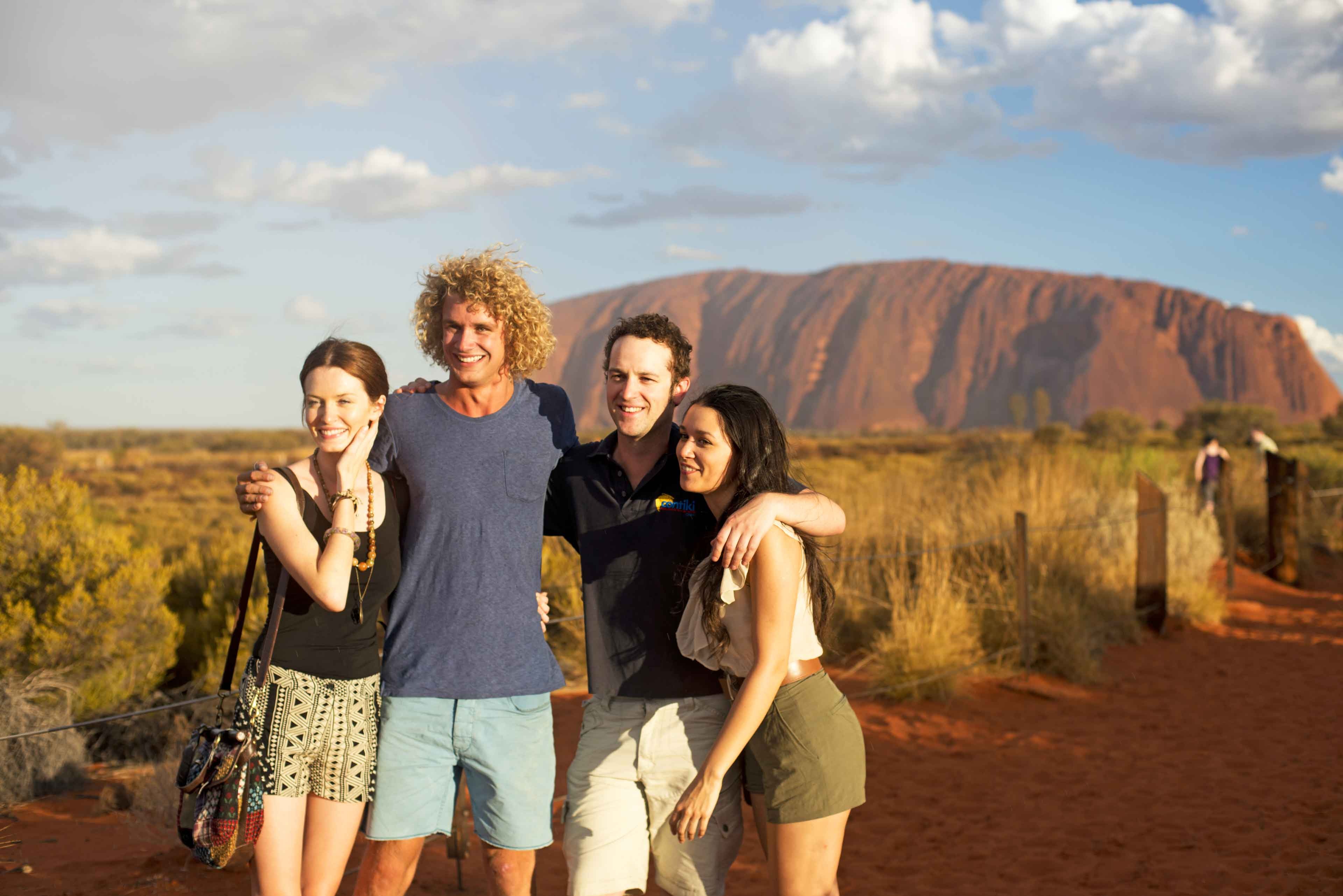 Group of travellers posing for a photo in front of Uluru on a desert in Australia 
