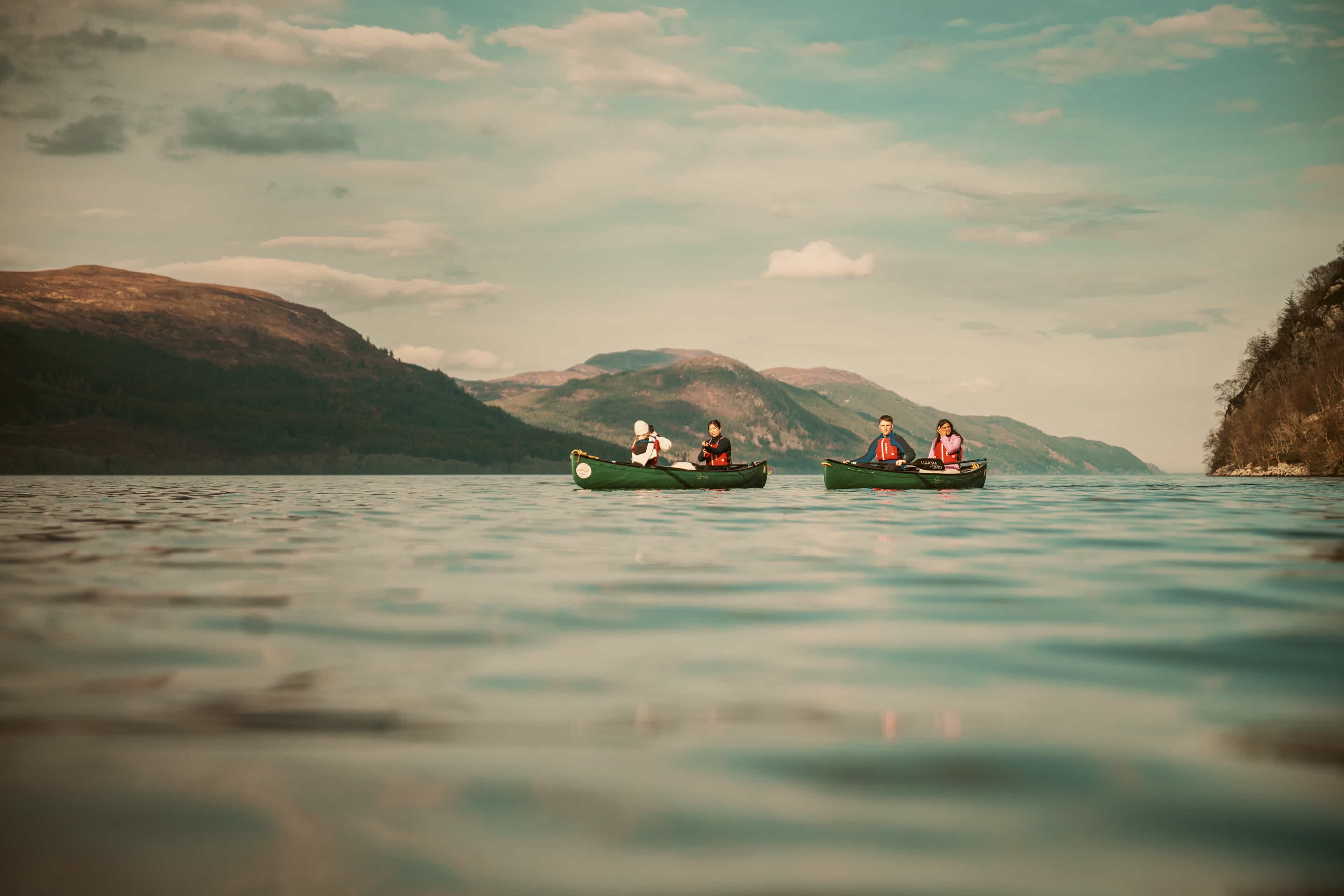 Travellers canoeing across a Scottish loch surrounded by rolling hills.