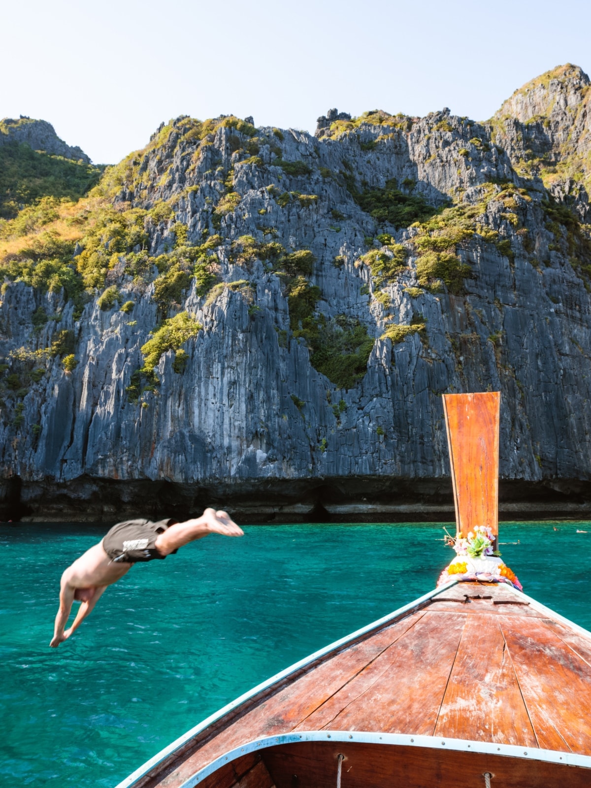 Traveller diving from a traditional longtail boat into turquoise water surrounded by limestone cliffs in Thailand.