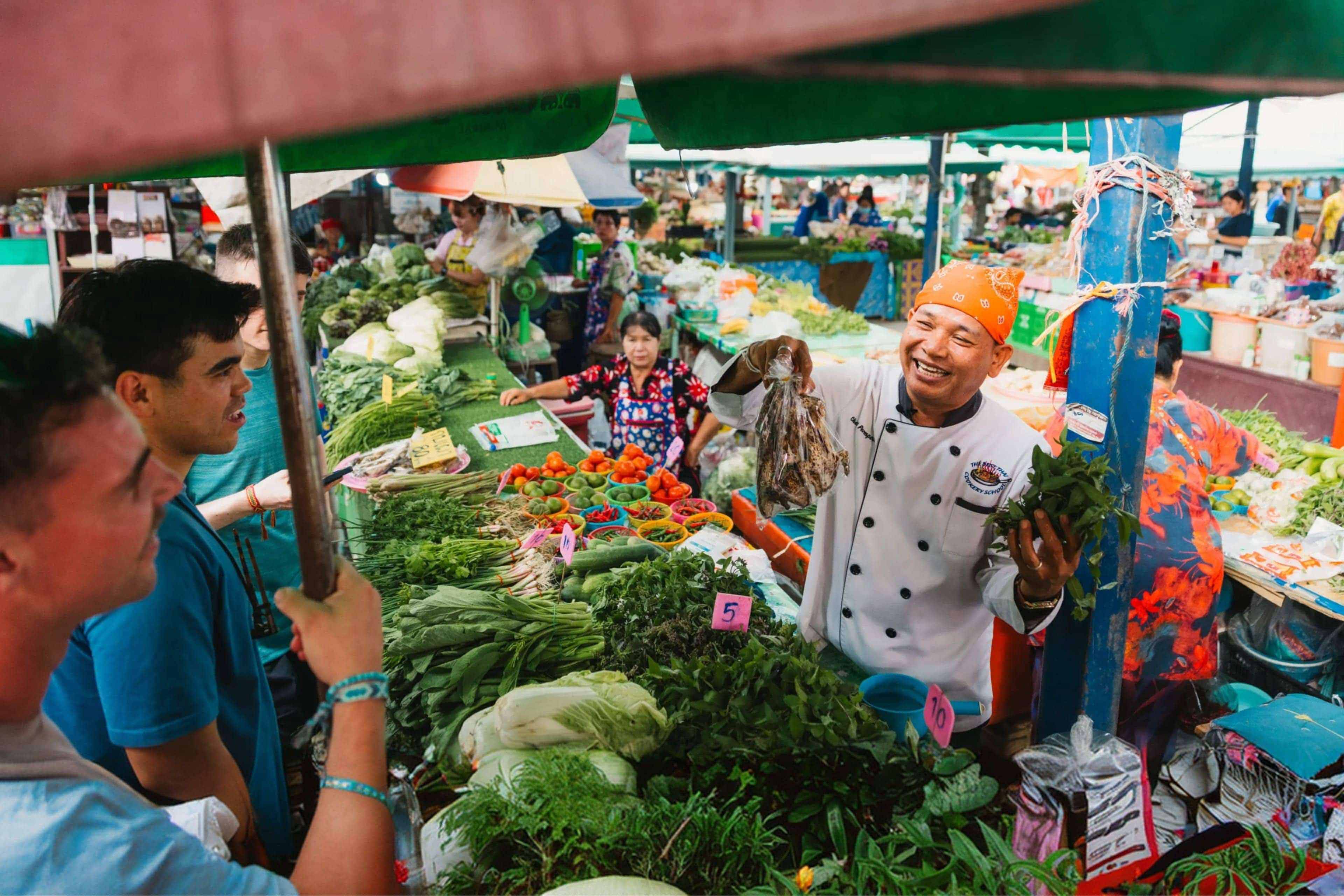 Travellers exploring a local food market with a guide in Thailand, discovering fresh produce and regional ingredients.