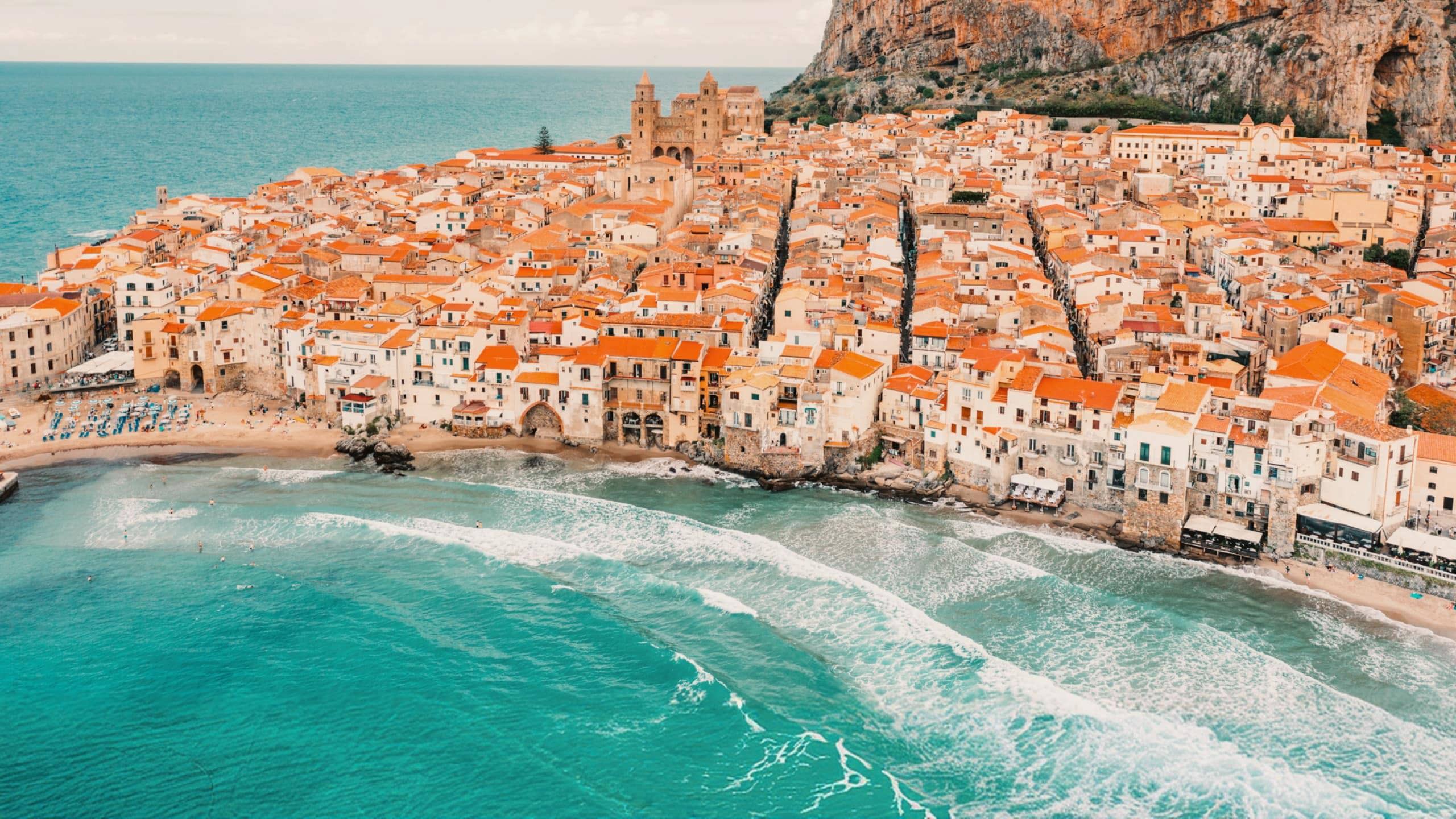 Aerial view of Cefalù's historic coastline and sandy beach in Sicily on the Contiki Best of Italy with Sicily Tour