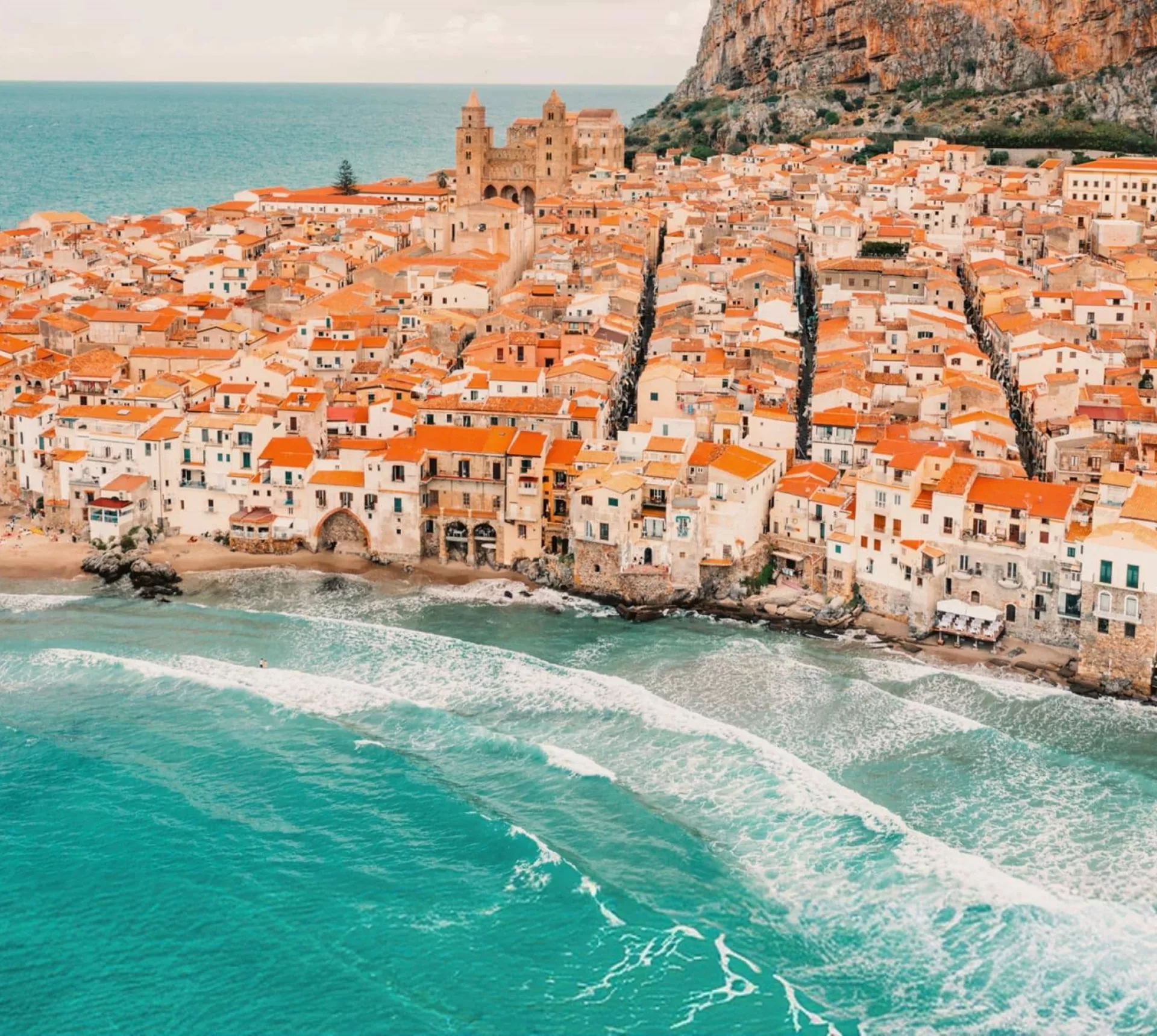 Aerial view of Cefalù's historic coastline and sandy beach in Sicily on the Contiki Best of Italy with Sicily Tour