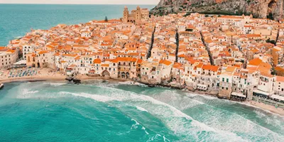 Aerial view of Cefalù's historic coastline and sandy beach in Sicily on the Contiki Best of Italy with Sicily Tour