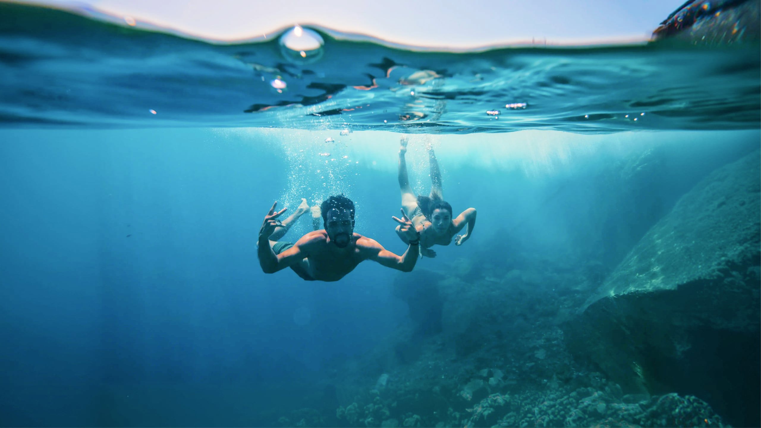 Two young travellers freediving underwater making peace signs in the clear blue waters of the Greek Islands - Contiki Athens and Santorini island hopper Tour