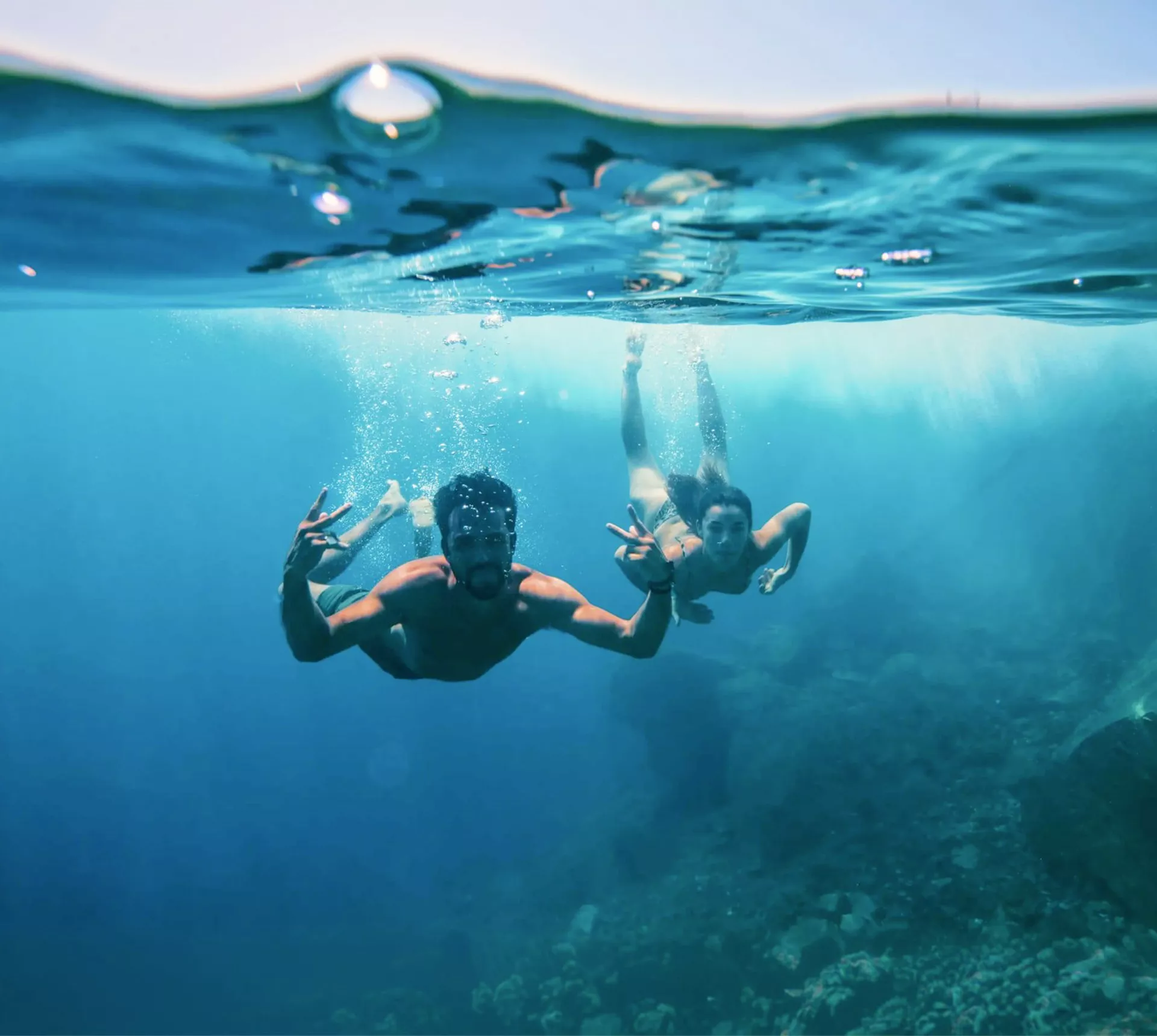 Two young travellers freediving underwater making peace signs in the clear blue waters of the Greek Islands - Contiki Athens and Santorini island hopper Tour
