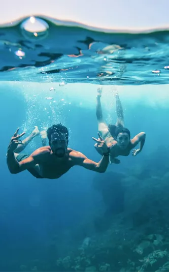 Two young travellers freediving underwater making peace signs in the clear blue waters of the Greek Islands - Contiki Athens and Santorini island hopper Tour