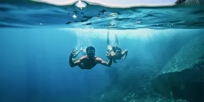 Two young travellers freediving underwater making peace signs in the clear blue waters of the Greek Islands - Contiki Athens and Santorini island hopper Tour