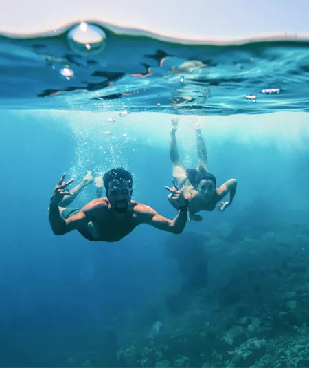 Two young travellers freediving underwater making peace signs in the clear blue waters of the Greek Islands - Contiki Athens and Santorini island hopper Tour