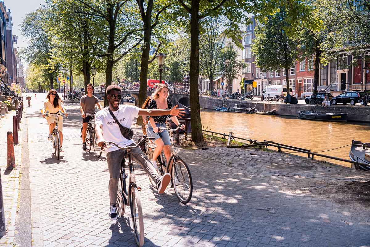 People On Bikes In Amsterdam Cycling Along Canal