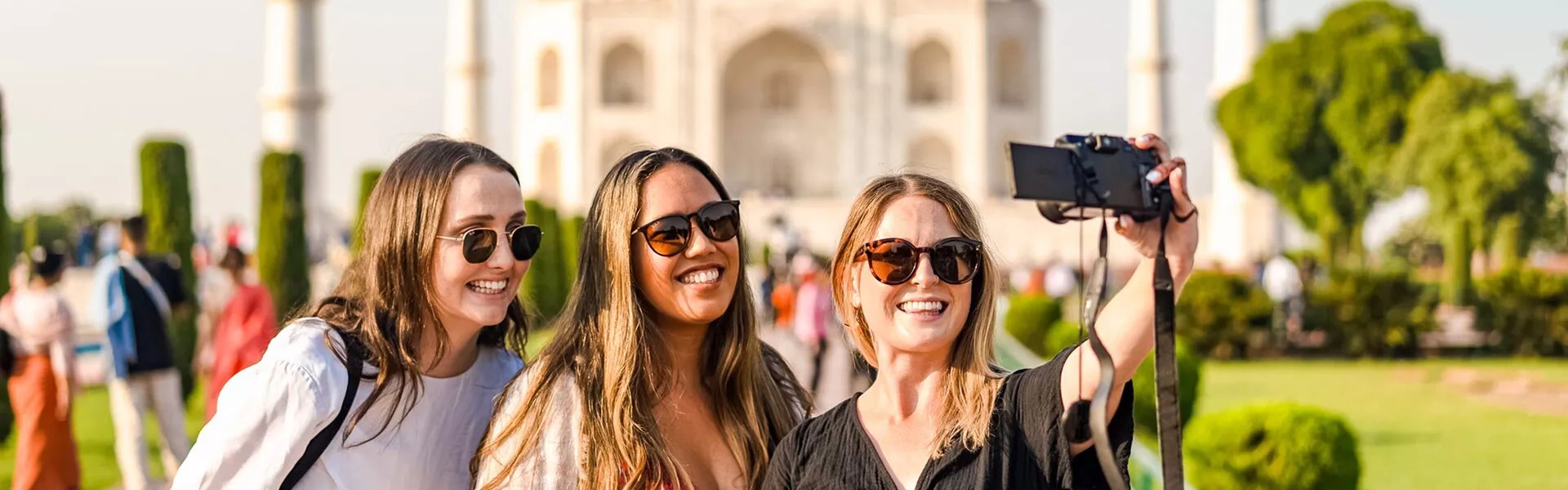 Three friends taking a selfie The Indian Taj Mahal as a background.
