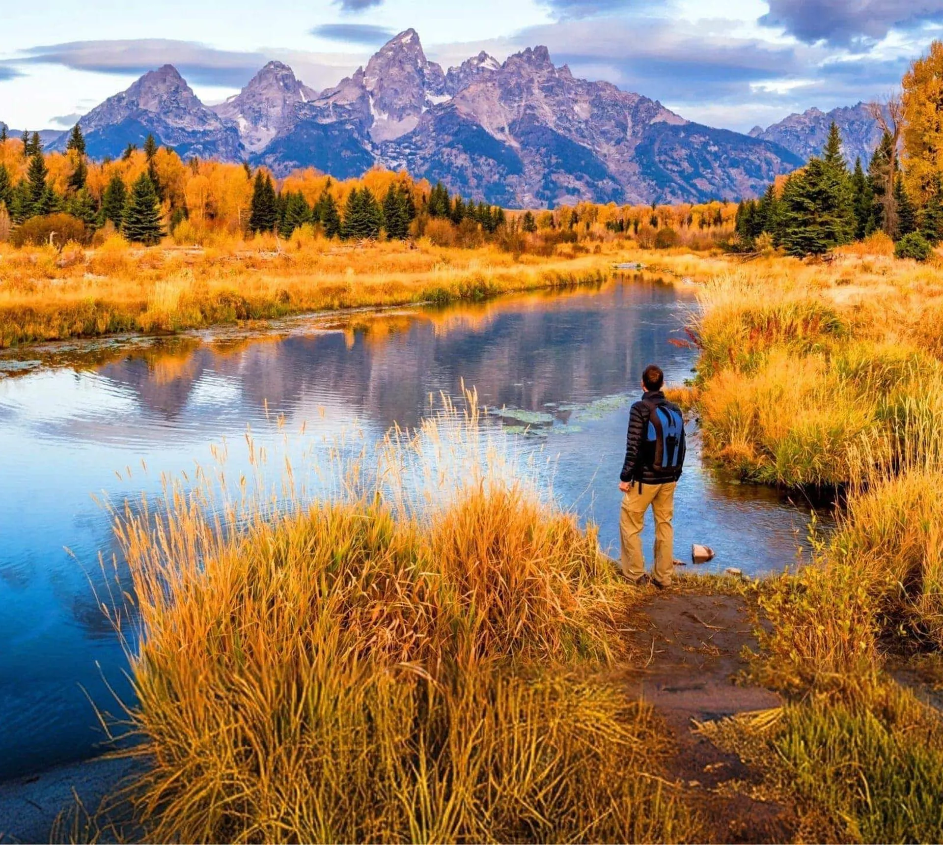 A traveller stands beside a river overlooking the Grand Teton mountains in Wyoming, surrounded by autumn colours - Contiki Active Yellowstone & Grand Tetons Tour