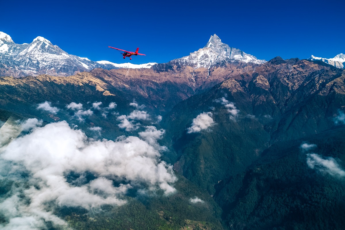 A small red place flying over high mountains in Nepal.