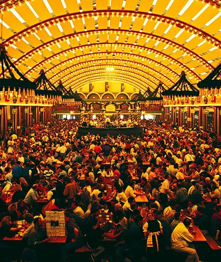 Packed Oktoberfest beer hall tent with ornate vaulted ceiling and thousands of revellers at long wooden tables in Munich Germany - Contiki Oktoberfest Tour
