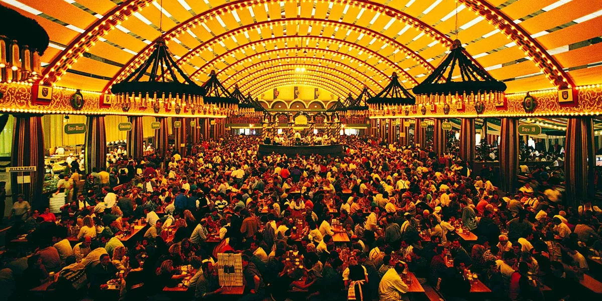 Packed Oktoberfest beer hall tent with ornate vaulted ceiling and thousands of revellers at long wooden tables in Munich Germany - Contiki Oktoberfest Tour