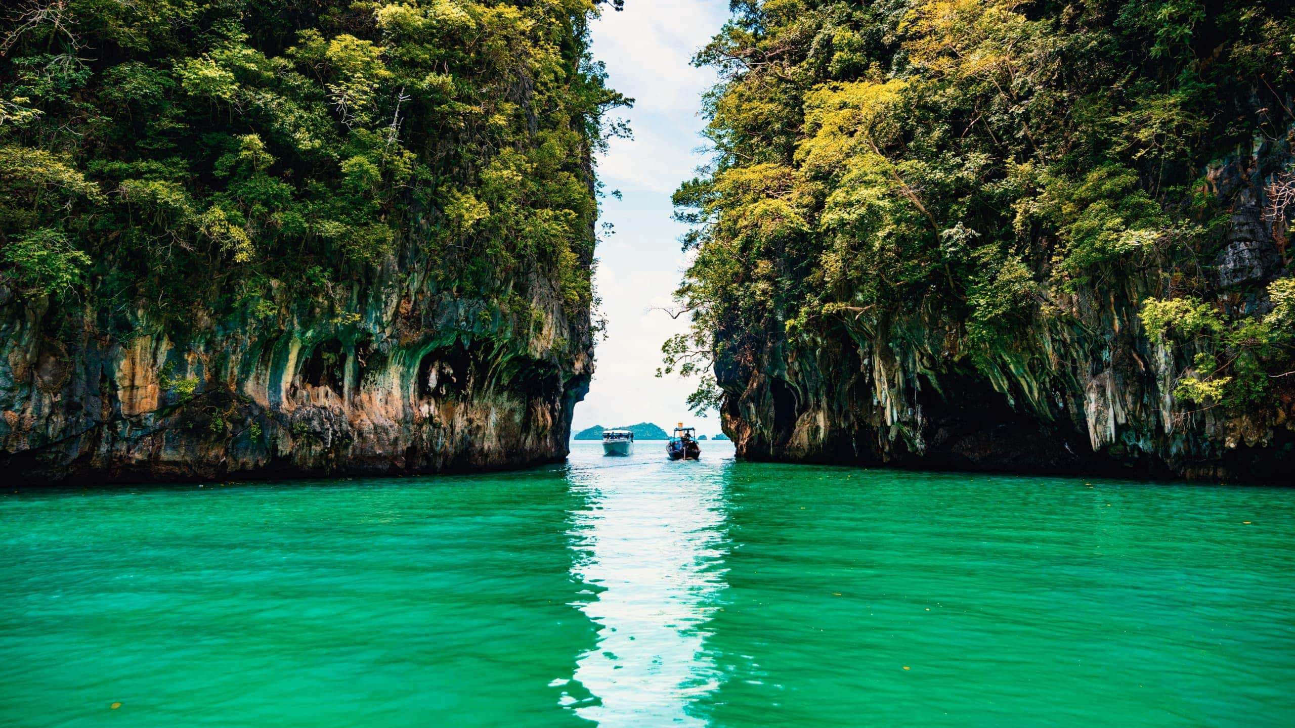 Longtail boats between towering limestone cliffs in the emerald waters of Phang Nga Bay Thailand - Contiki Thai Island Hopping West