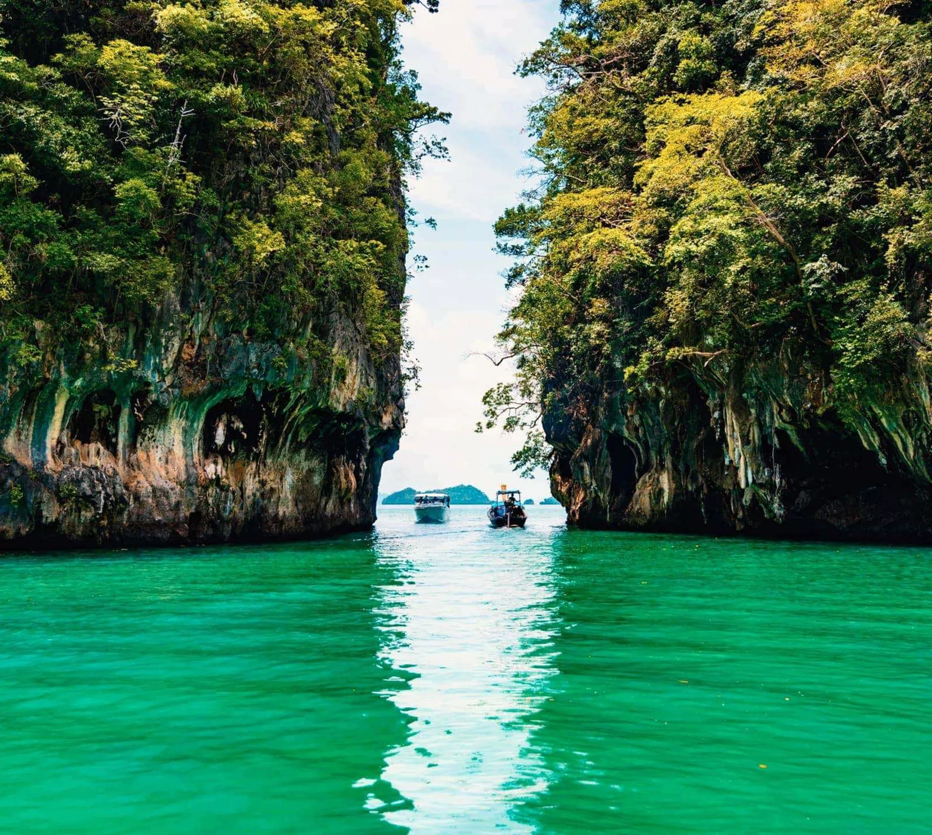Longtail boats between towering limestone cliffs in the emerald waters of Phang Nga Bay Thailand - Contiki Thai Island Hopping West